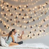 a man and woman sitting on top of a bed next to a string of lights