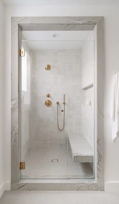 a walk in shower sitting next to a white wall and tiled floor with gold fixtures