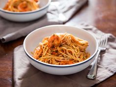 two bowls filled with pasta and shrimp on top of a table next to silverware