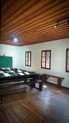 an empty room with tables and benches on the floor in front of two large windows