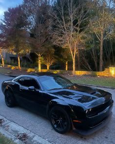 a black car is parked on the side of the road in front of some trees