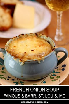 a french onion soup in a blue bowl on a plate next to a glass of wine