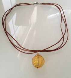 See the beauty of Murano glass and precious metals in a simple and distinctive design.  The large bead, an exquisite yellow crystal encasing 24kt gold foil, measures 20mm in diameter (25/32 in).  The metallic leather cords complement the fresh and modern look.  This necklace can be made as a choker if you choose to have it short.  This is a very modern, simple  and minimal piece of jewelry.   Additional Components: - Vermeil heishi bead - Metallic red leather cords - 14kt gold filled: wire suspe Handmade Gold Glass Jewelry, Round Murano Glass Gold Jewelry, Gold Glass Jewelry Wire Wrapped, Elegant Glass Jewelry With Wire Wrapping, Elegant Glass Wire Wrapped Necklaces, Gold Murano Glass Jewelry As Gift, Gold Murano Glass Jewelry For Gifts, Gold Murano Glass Jewelry Gift, Gold Glass Pendant Necklace