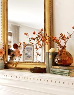 a mirror sitting on top of a mantle next to a vase with flowers in it