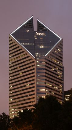 a very tall building with some lights on it's sides and trees in the foreground