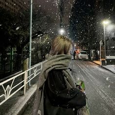 a woman walking down the street at night in the snow with her scarf around her neck