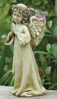 an angel figurine with flowers in her hands on top of a stone wall