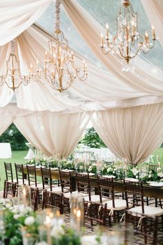 the tables are set up for a wedding reception with chandeliers and white draping