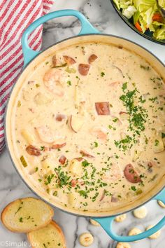 a blue pot filled with shrimp and potato chowder next to some crackers on the side