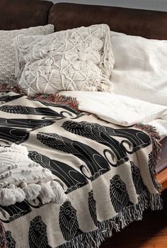 an unmade bed with white and black blankets on it's headboard, next to a brown couch