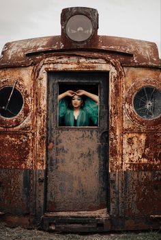 a woman is standing in the doorway of an old rusted out truck with her hands on her head