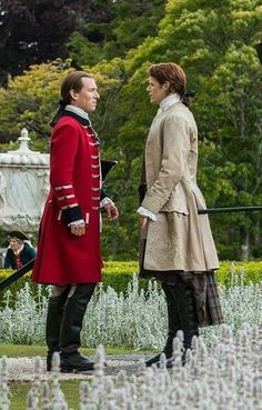 two people dressed in period clothing standing next to each other on a field with white flowers