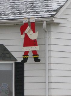 a christmas decoration hanging from the side of a white house with a santa clause on it