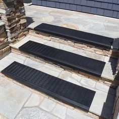 three black doormats sitting on the steps in front of a stone wall and building