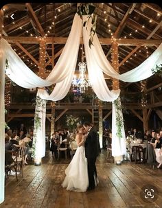 a bride and groom kissing in front of their wedding party at the reception hall with white draping