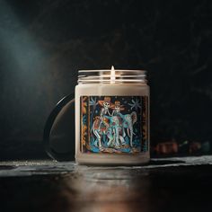 a candle with a painting on it sitting on a table next to other items and candles