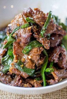 a white bowl filled with meat and greens on top of a tablecloth covered table