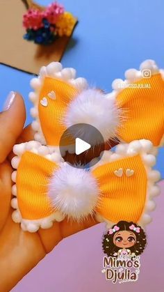 an orange bow with white pom - poms is held in someone's hand