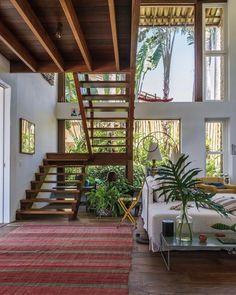 a living room with stairs leading up to the second floor and potted plants on the other side