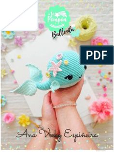 a hand holding a small knitted doll with flowers on it's head and the word