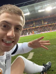 a man sitting on top of a soccer field with his hand out in front of him