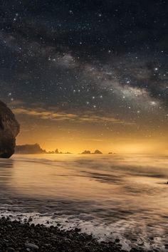 the stars are shining in the night sky over the water and rocks on the beach