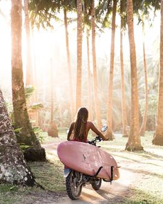 a woman on a motor bike with a surfboard strapped to the handlebars