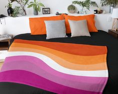 a bed with black, orange and pink sheets in a room filled with potted plants