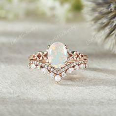 a white opal and diamond ring sitting on top of a pine tree