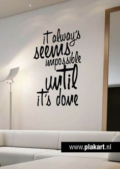 a living room with a white couch and black wall decal that says it always seems impossible until it's done