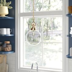 a kitchen sink under a window with blue walls and shelving above it, along with hanging glass globe lights