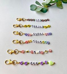 six keychains with beads and charms on them sitting next to a green plant