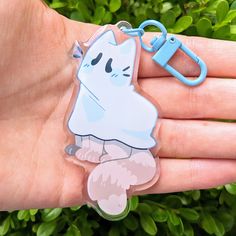 a hand holding a blue and white cat shaped keychain on it's palm