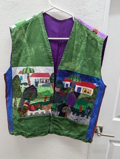 a green vest hanging on a door with houses and farm animals painted on the front