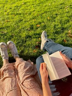 a person laying on the grass reading a book with their feet up in the air