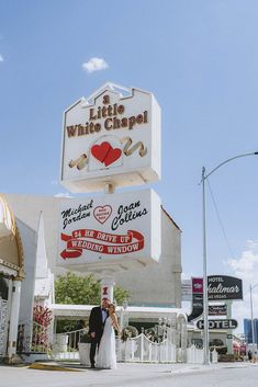 a bride and groom pose in front of the white chapel sign at their wedding venue