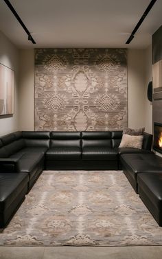 a living room with black leather couches and a large rug in front of the fireplace