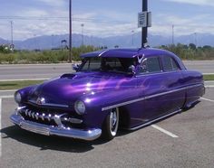 an old purple car parked in a parking lot