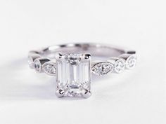 an emerald cut engagement ring with diamonds on the band and side stones in white gold