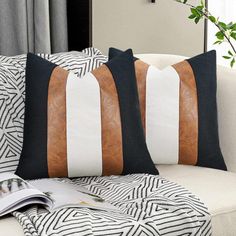 two black and white pillows sitting on top of a couch next to a plant in a vase