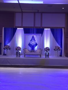 the stage is set up for an event with blue lighting and white drapes on it