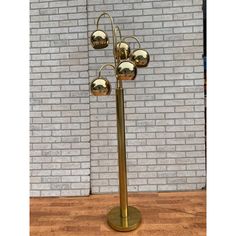 a golden metal lamp with four balls on it's stand against a brick wall