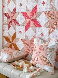 a quilted wall hanging next to pillows on a bench with pom poms