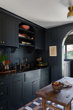 a kitchen with black cabinets and wooden table in front of the counter top, along with a checkered rug on the floor