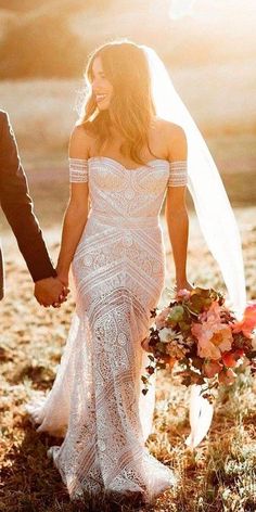 a bride and groom holding hands walking through the grass