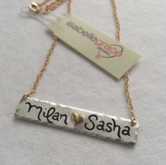 Double Name Bar Necklace - A gorgeous holiday gift, this is the perfect piece to layer with a longer necklace! The Double Name Bar Necklace features a (0.999) fine silver bar custom inscribed with two names or sets of initials separated by a 22kt gold heart. The edges are also slightly hammered to give it a distressed look. The name bar is approximately 1 3/4 inches long but the size may vary depending on personalization. Also has a matte finish! Artisan Gift Necklaces, Artisan Stamped Necklace Gift, Handmade Adjustable Name Necklace For Anniversary, Handmade Nameplate Necklace As Personalized Gift, Handmade Adjustable Nameplate Necklaces, Artisan Stamped Necklace As Gift, Artisan Stamped Necklace For Gift, Handmade Nameplate Necklace For Personalized Gift, Engraved Nameplate Necklaces