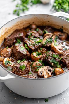 a pot full of stew with mushrooms and parsley on the side, ready to be eaten