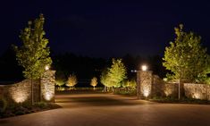 an entrance to a home at night with lights on and trees lining the driveway area