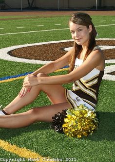 a young woman sitting on the ground with her legs crossed and cheerleader's pom - poms around her ankles