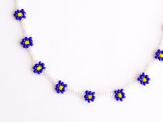 a beaded necklace with blue and yellow flowers on white beads is displayed against a white background